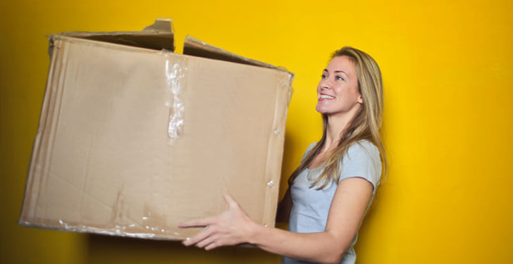 reasons to move to colorado blonde woman holding large cardboard box yellow background